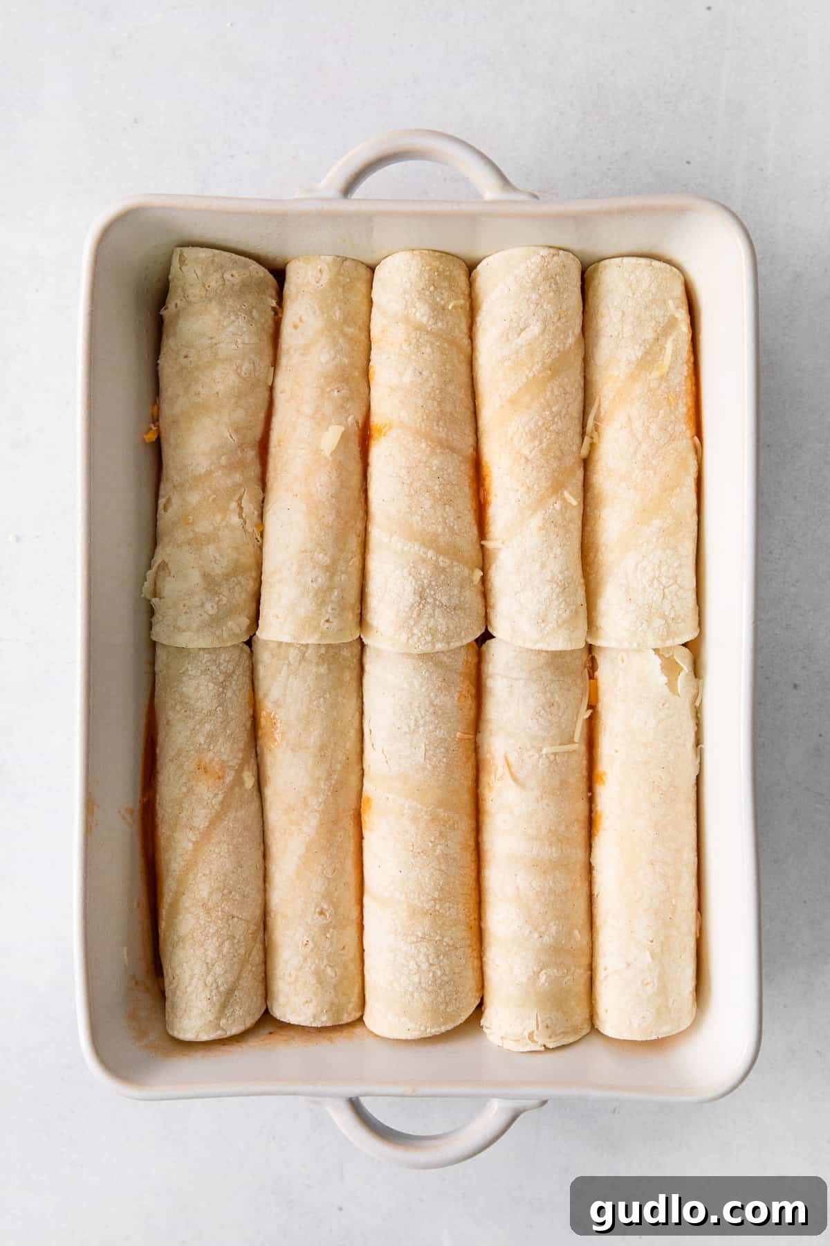 Rolling and Assembling Cheese Enchiladas Cheese enchiladas being rolled and placed into a casserole dish, ready for baking.