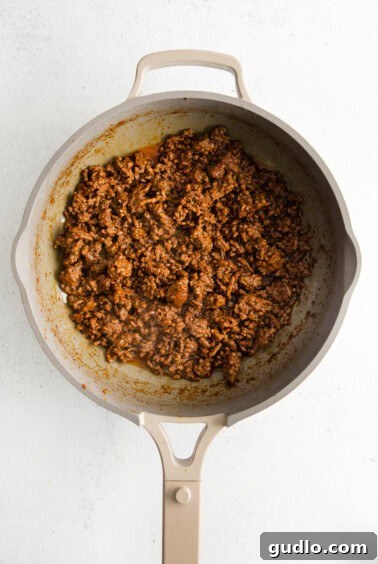 Ground beef cooking in a skillet with taco seasoning and beef broth.