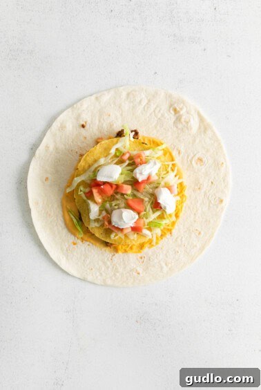 A tortilla filled with layers of beef, cheese, tostada, and fresh vegetables.