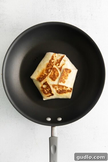 A crunchwrap supreme searing in a hot skillet until golden brown.