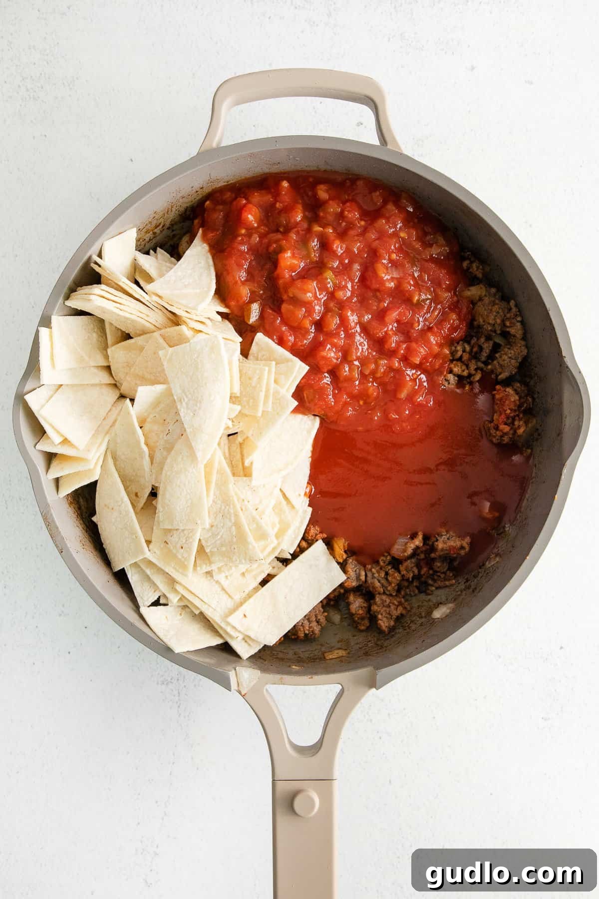 Cheesy Taco Bake 6 Salsa and tortilla strips mixed into the seasoned ground beef in a skillet for taco bake.