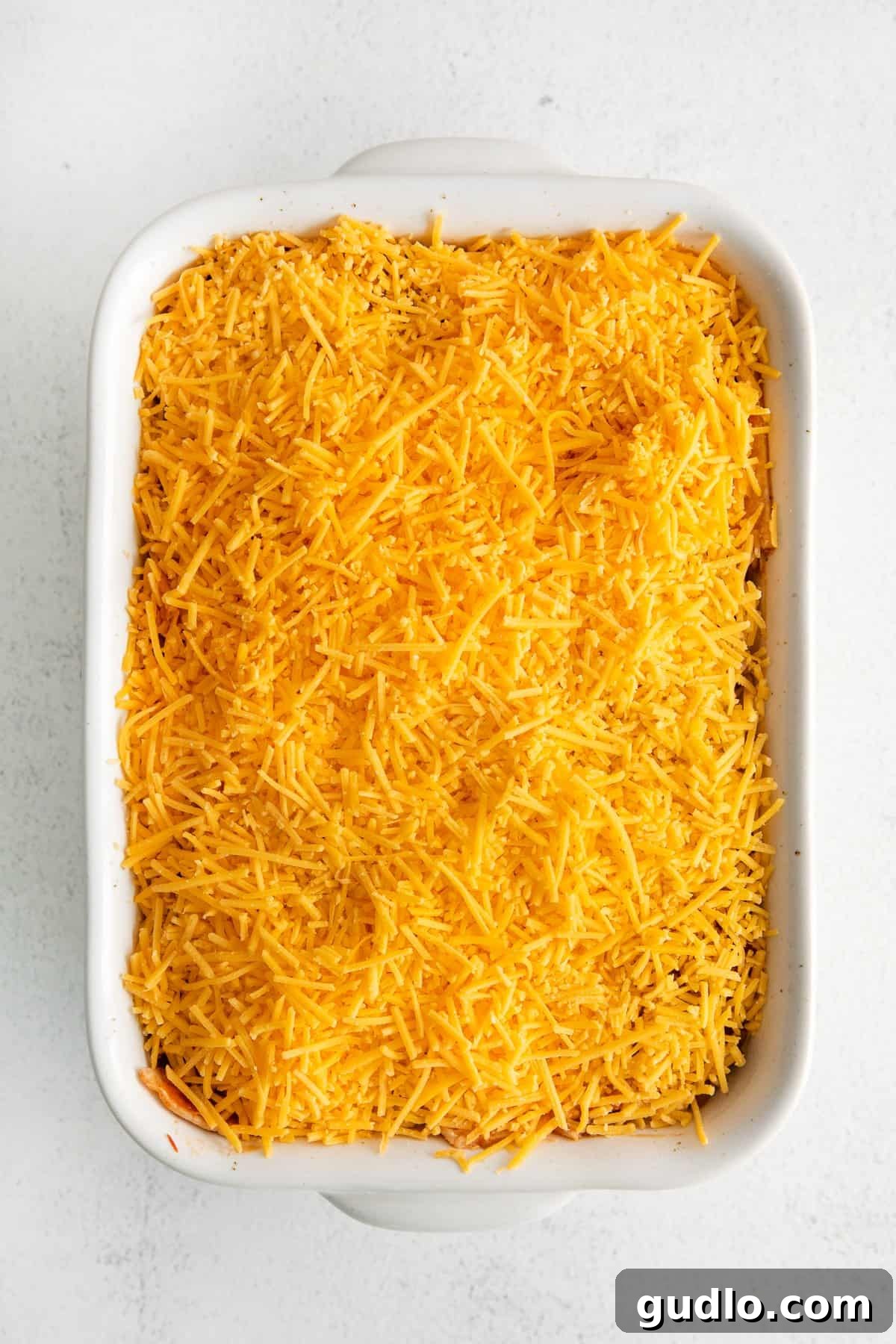 Cheesy Taco Bake 8 Taco bake in a casserole dish topped with an even layer of shredded cheddar cheese, ready for baking.