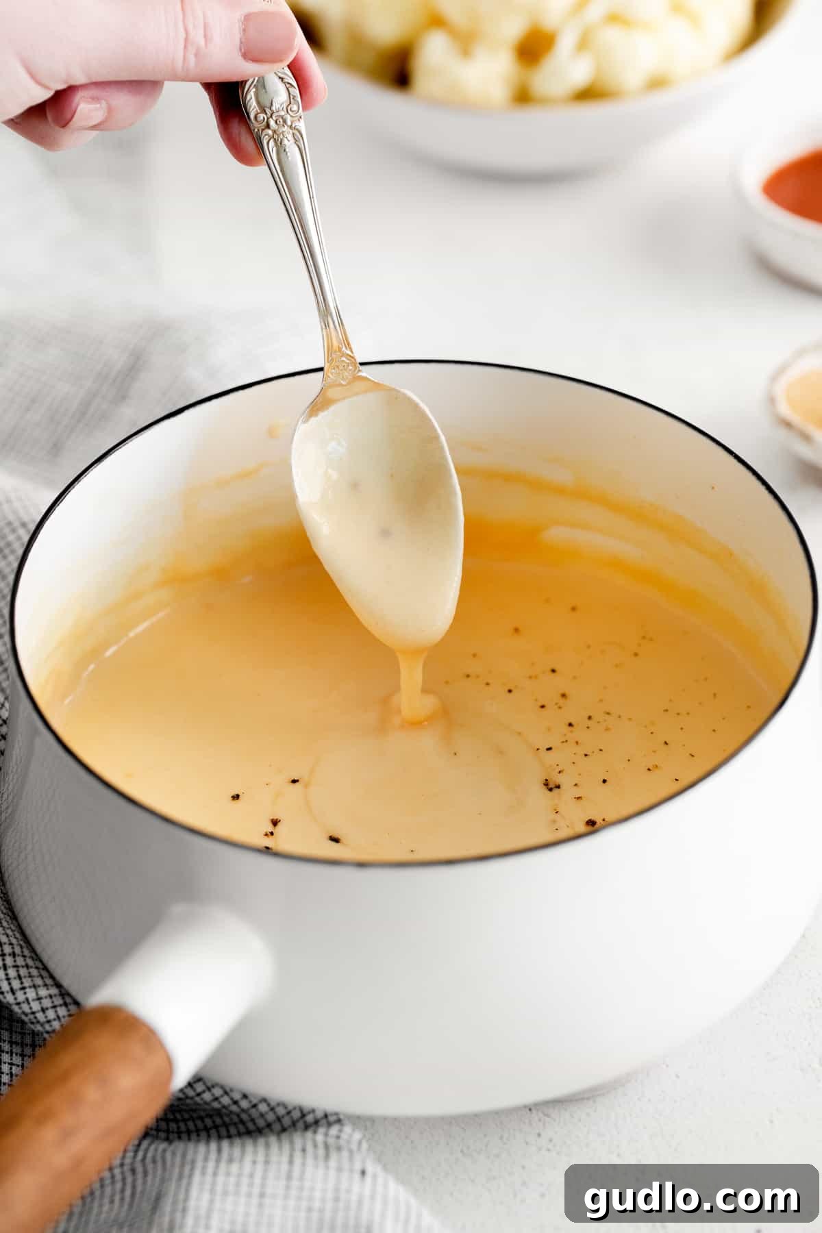 Rich, golden cheddar cheese sauce simmering in a pot, showcasing its smooth and creamy texture, ready to be served and enjoyed.