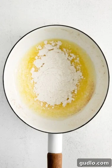 Flour being whisked into melted butter in a pot, forming a pale blonde roux, the base for the cheese sauce.