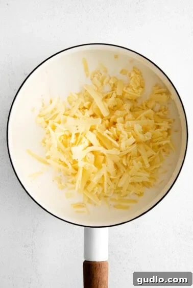 Freshly shredded cheese melting into a creamy roux base in a pot, stirred until smooth.