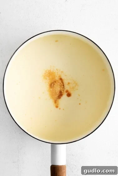 Granulated garlic and hot sauce being stirred into creamy cheese sauce in a pot, enhancing its flavor profile.