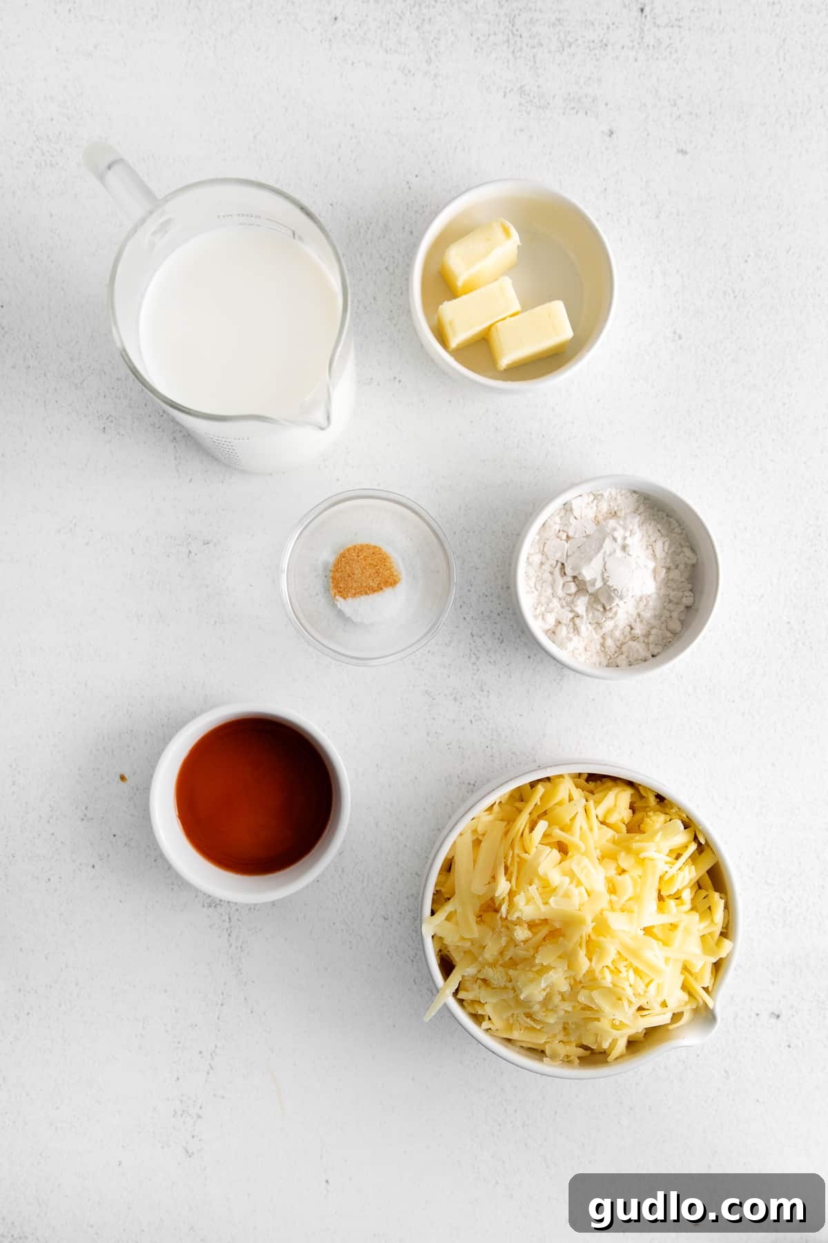 An inviting assortment of fresh ingredients laid out on a clean countertop, including a generous block of white cheddar cheese, a jug of milk, butter, and various spices, all ready for the preparation of a homemade cheese sauce.