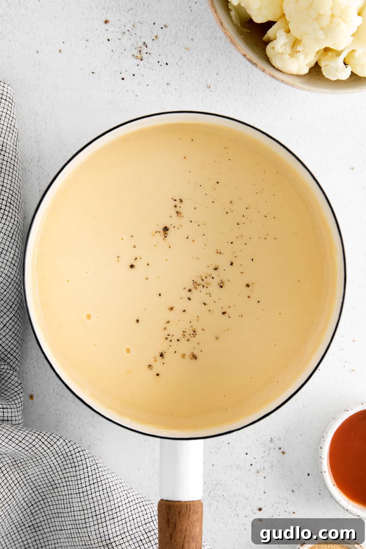 Close-up of freshly made cheddar cheese sauce in a pot, beautifully garnished with a touch of freshly cracked black pepper, showcasing its rich texture and inviting appearance, ready to be enjoyed.