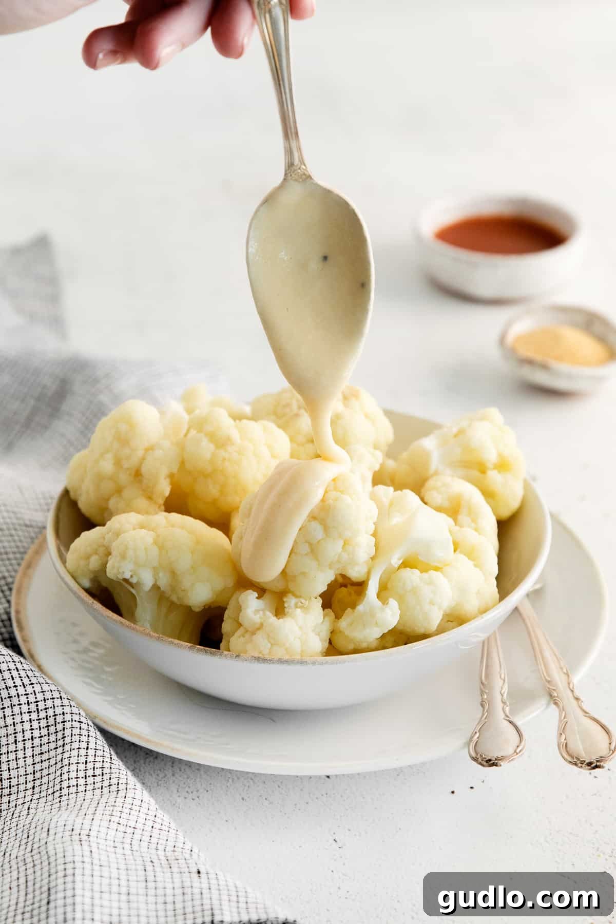 A generous serving of rich, creamy cheddar cheese sauce elegantly drizzled over freshly steamed cauliflower florets, garnished with vibrant fresh herbs, showcasing its perfect application as a topping.