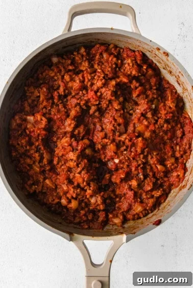 Creamy Bechamel Lasagna 6 Rich meat sauce simmering in a skillet, combining tomatoes, ground beef, and spices.