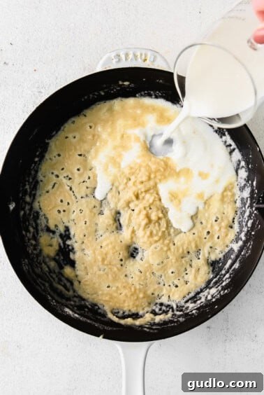 Creamy Bechamel Lasagna 8 A hand pouring milk into a saucepan, whisking to combine with the roux for bechamel sauce.