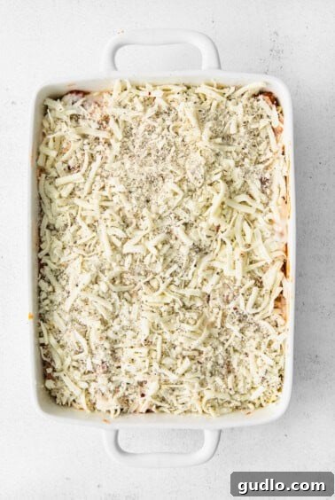 Creamy Bechamel Lasagna 12 A casserole dish filled with unbaked lasagna, topped with a generous layer of shredded cheese.