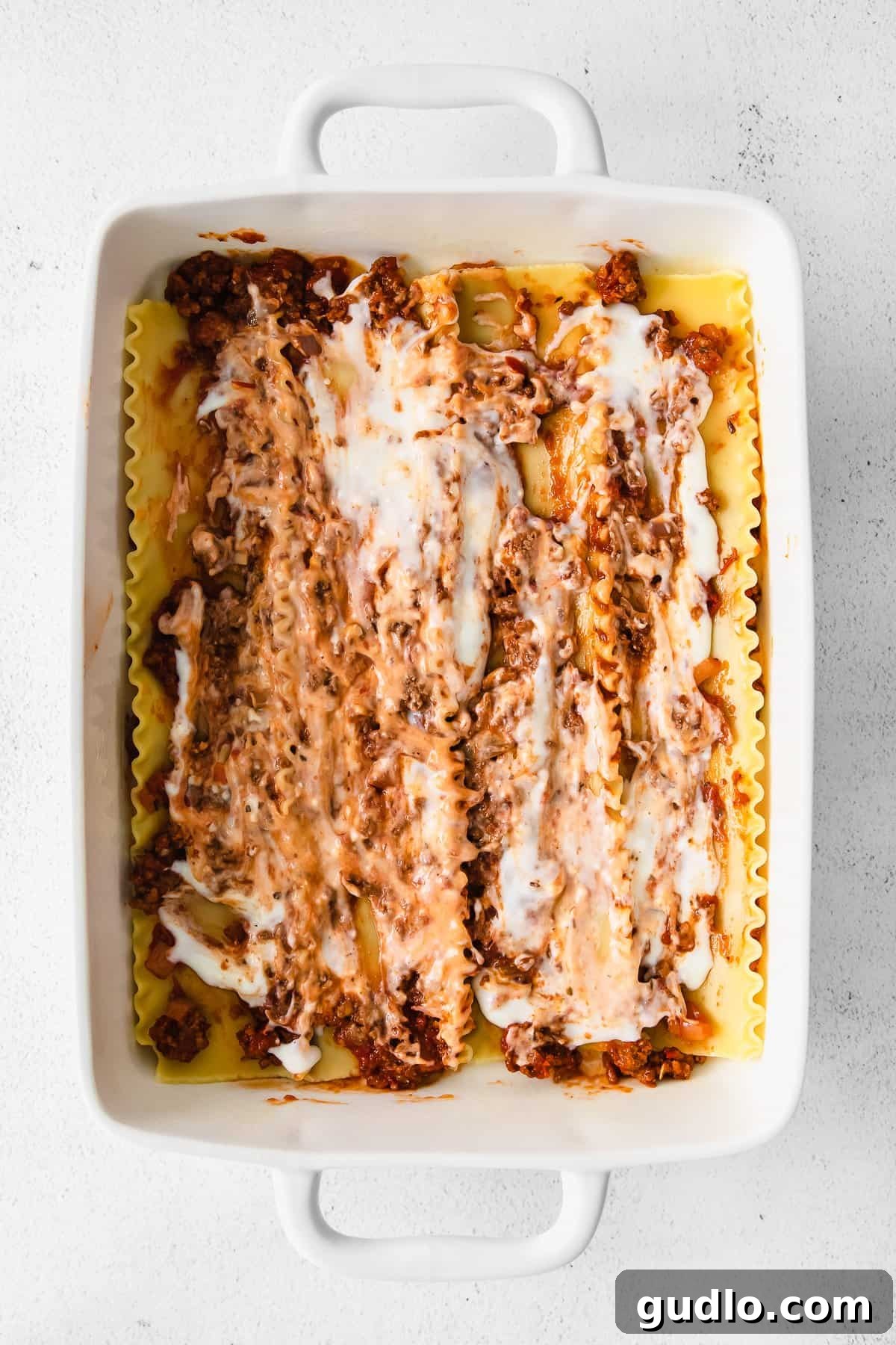 Lasagna Layers Assembled A partially assembled lasagna in a white casserole dish, showing layers of noodles and sauce before baking.