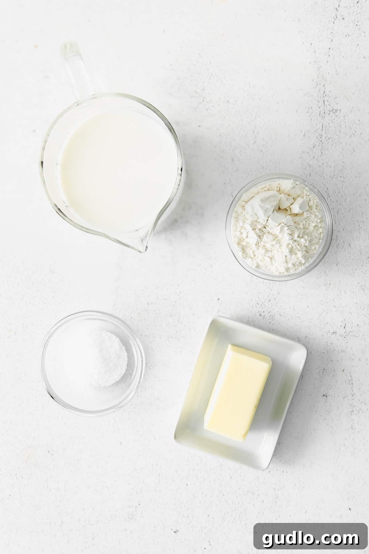 Learn how to make a creamy, white bechamel sauce recipe with just 3 basic ingredients - butter, flour, and milk. Three essential ingredients - butter, flour, and milk - laid out on a kitchen countertop.
