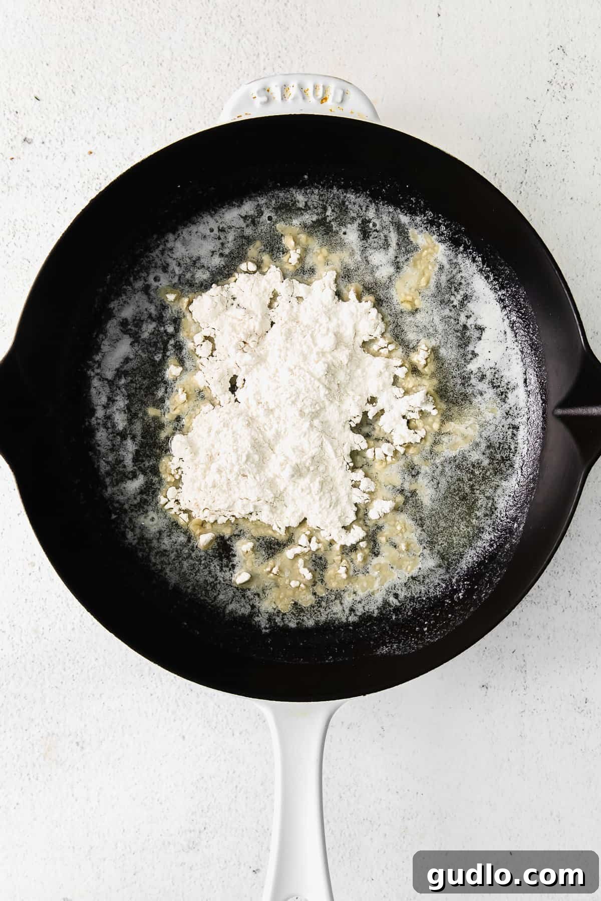 Learn how to make a creamy, white bechamel sauce recipe with just 3 basic ingredients - butter, flour, and milk. A chef meticulously making a white roux in a cast iron pan, showing the butter and flour combining.