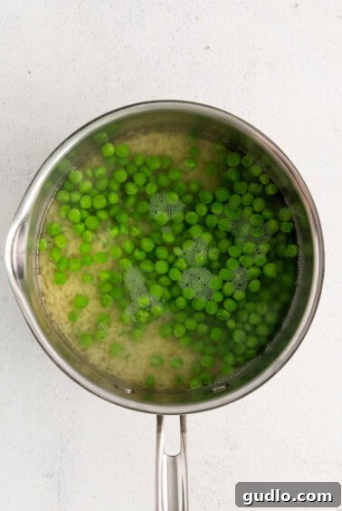 Fresh green peas in a colander, having been blanched, with orzo in a pan on a white surface.