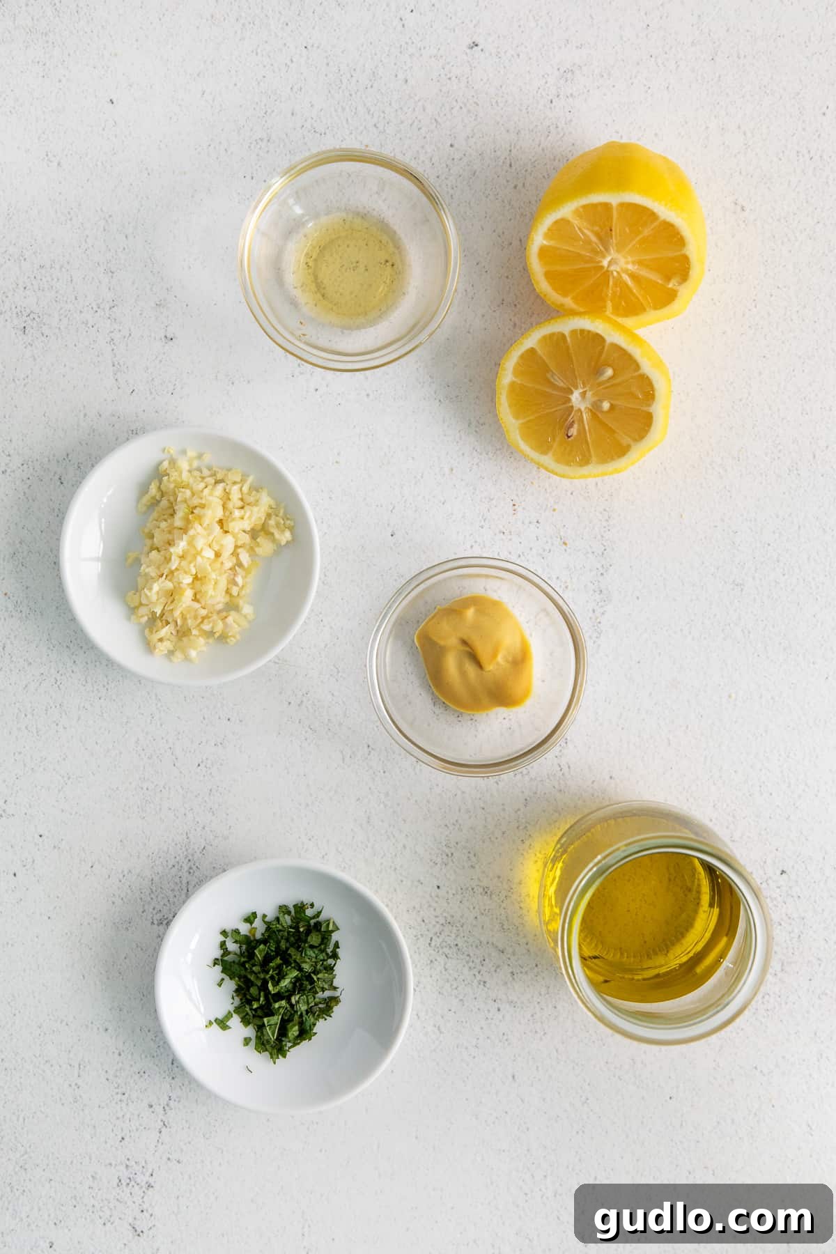 Various ingredients for a lemon vinaigrette, including olive oil, lemon, garlic, and herbs, arranged in small bowls.
