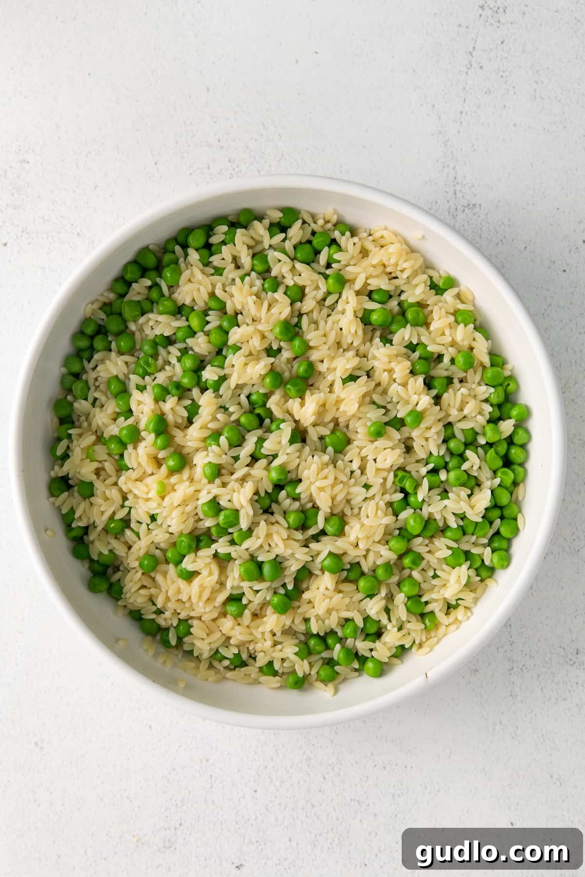 Close-up of vibrant green peas and orzo pasta in a white bowl, capturing their fresh texture.