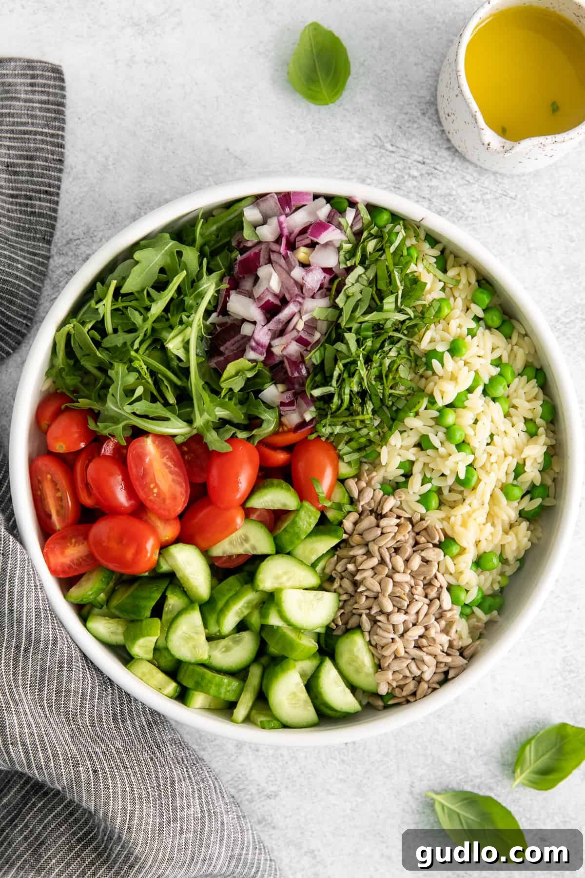 A large white bowl filled with a beautifully mixed lemon orzo salad, showcasing fresh vegetables and creamy goat cheese.
