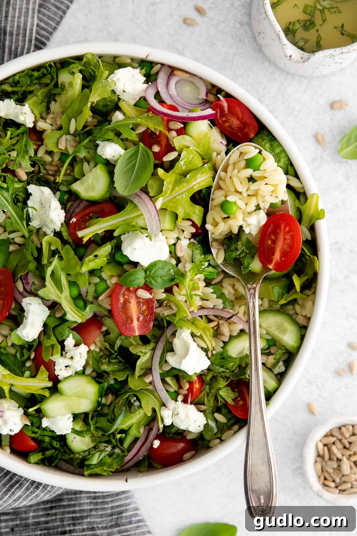 A beautifully presented lemon orzo salad with goat cheese, ready for serving, in a large white serving bowl with a spoon.