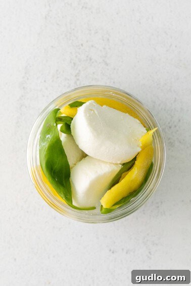 Goat cheese, lemon rind, and basil arranged in a jar.