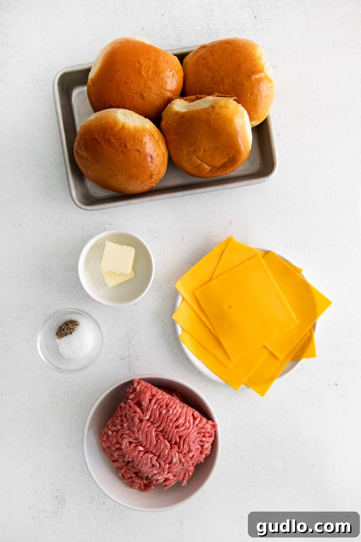 Essential Ingredients for Simple Cheeseburgers Fresh ingredients laid out for making cheeseburgers, including ground beef, buns, butter, salt, pepper, and cheese slices.