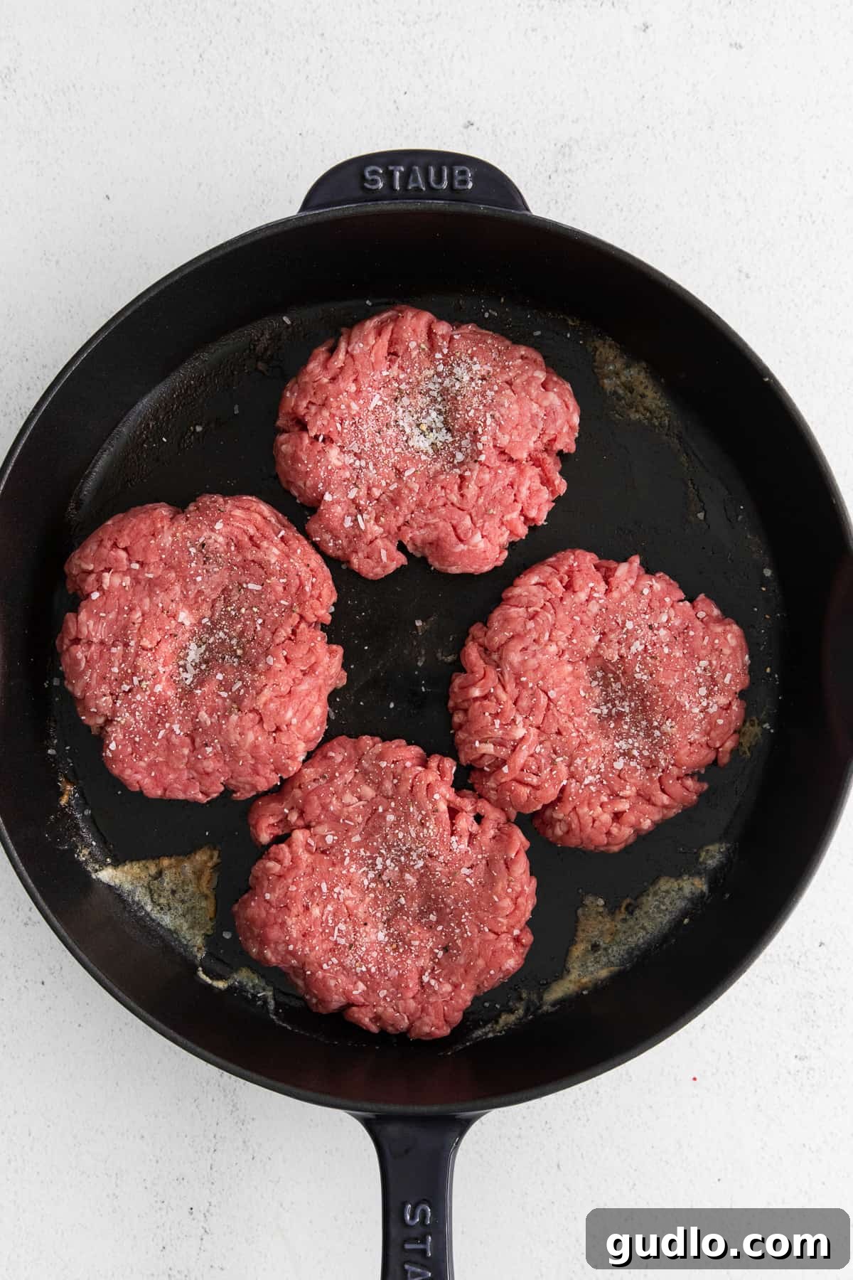 Cooking Burger Patties in a Skillet Four beef patties sizzling and cooking in a cast iron skillet.