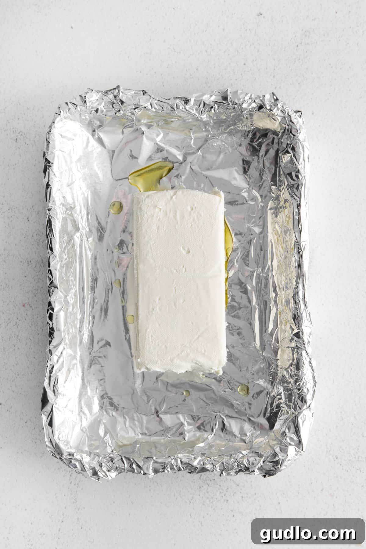Prepare your cream cheese by placing it in a sturdy aluminum foil boat. A firm block of cream cheese carefully placed into a neatly folded aluminum foil boat, ready for the next step of seasoning before smoking.