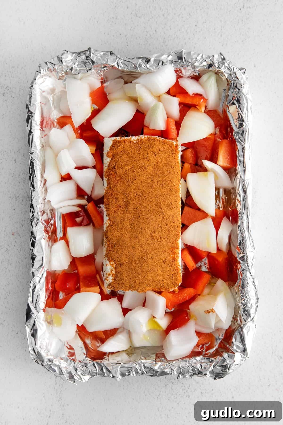 Surround your perfectly seasoned cream cheese with vibrant veggies for added flavor and visual appeal. A block of seasoned smoked cream cheese nestled in its aluminum foil boat, generously surrounded by a colorful array of fresh, chopped vegetables, ready to be placed into the smoker.