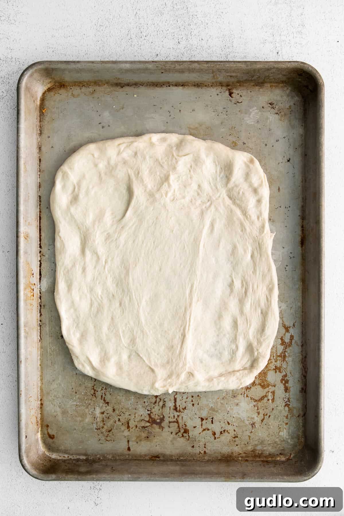 Unbaked Cheese Bread on Baking Sheet Unbaked cheese bread dough spread on a baking sheet, ready for the oven.