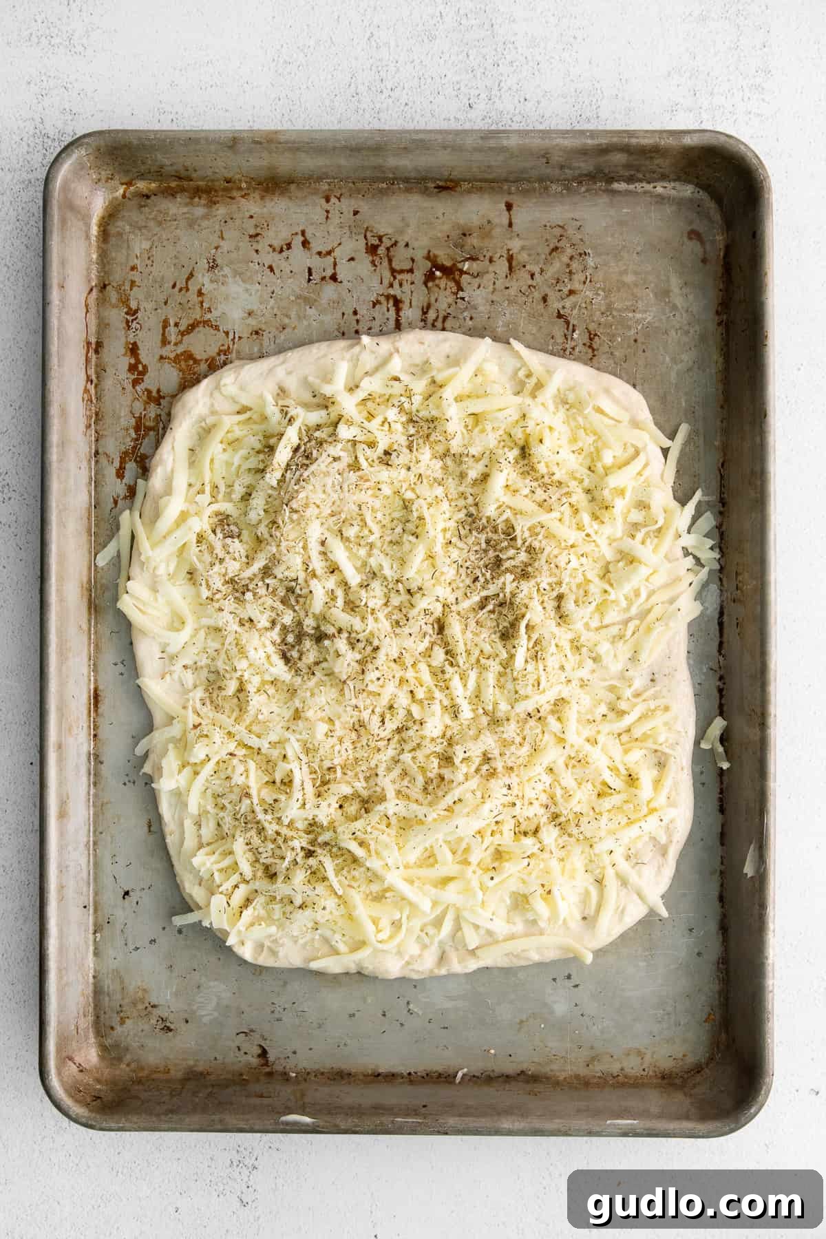 Pre-baked Cheesy Topping Close-up of cheese bread topped with mozzarella, parmesan, and Italian seasoning, ready to bake.