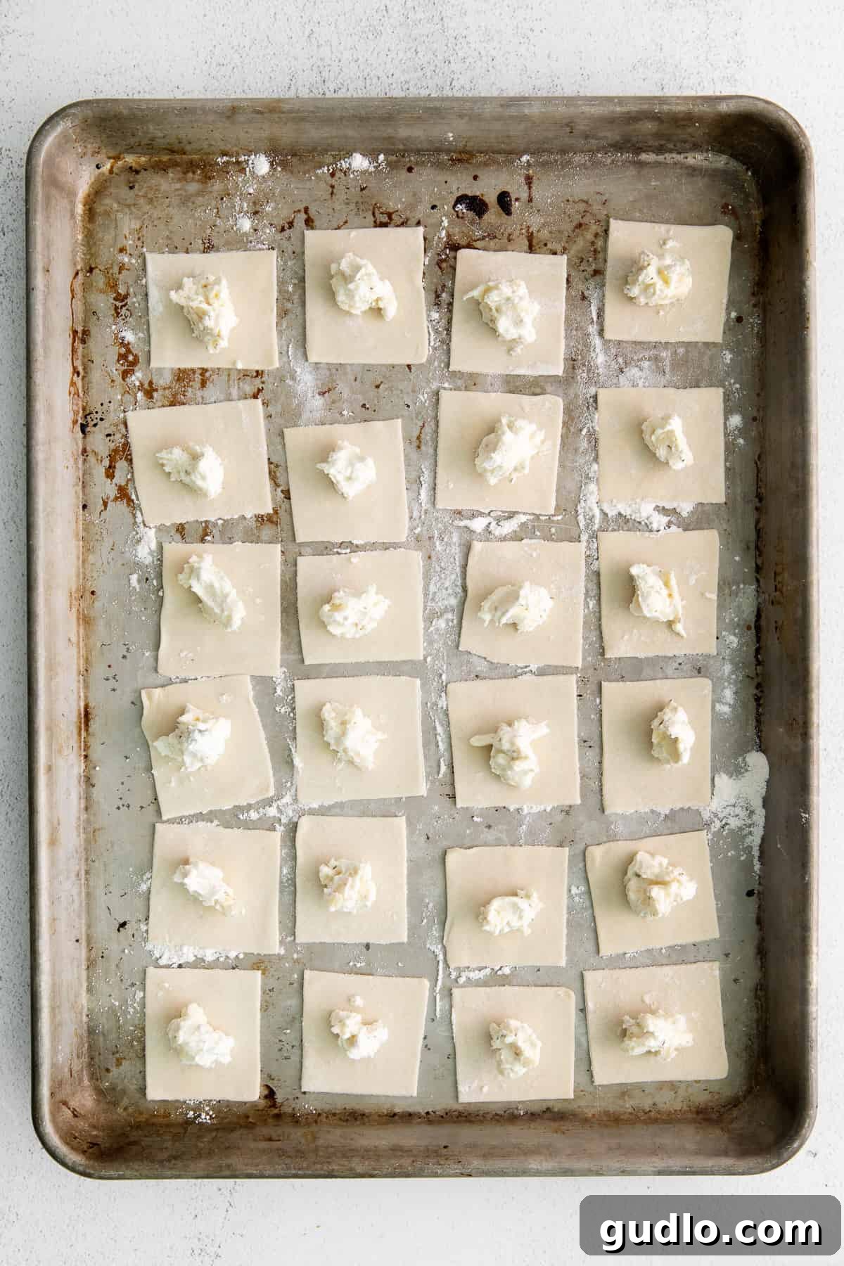 Hands demonstrating the folding process of shaping cheese tortellini from dough squares.