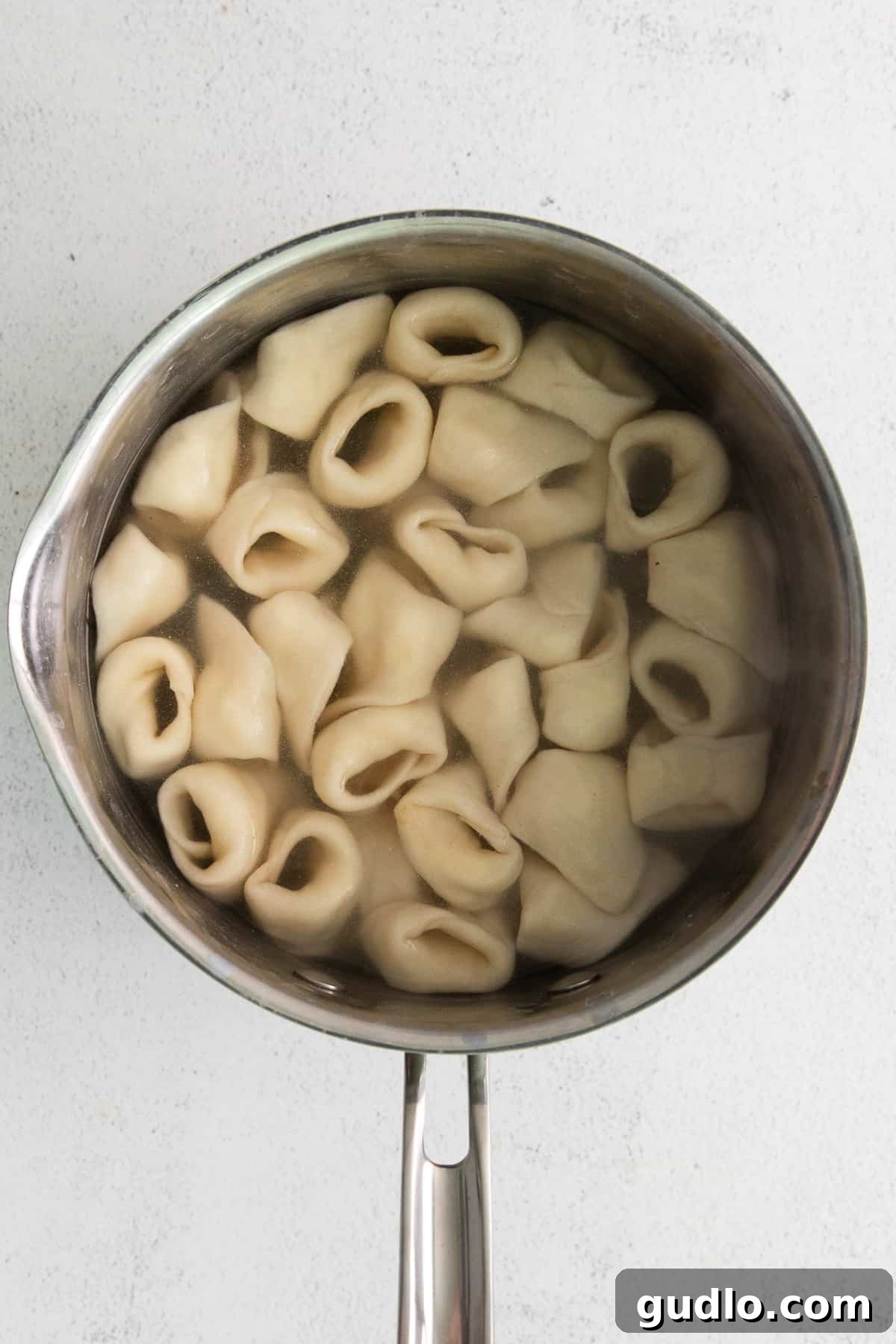 Homemade cheese tortellini being carefully dropped into a pot of boiling water.