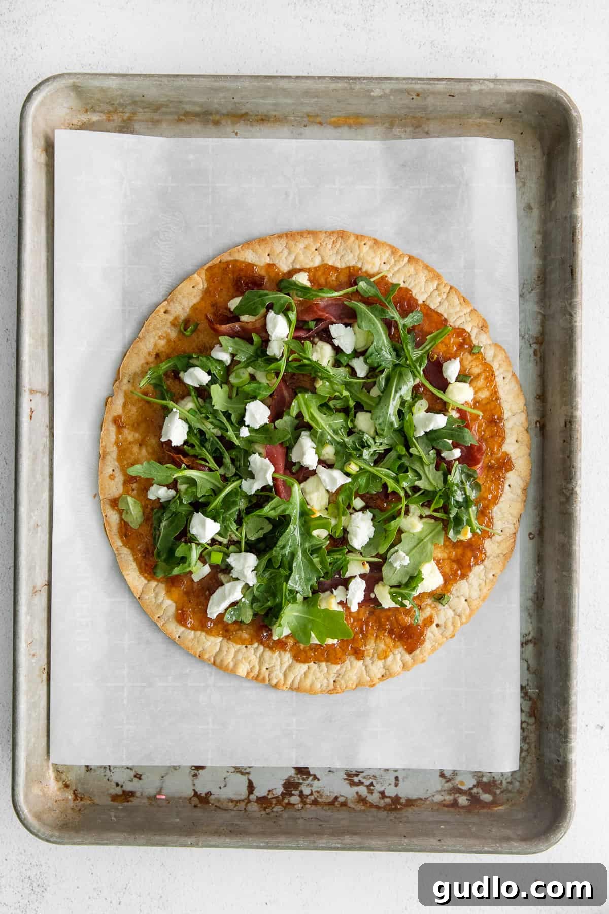 Finished Fig and Goat Cheese Flatbread with Arugula Freshly baked fig and goat cheese flatbread topped with a vibrant arugula salad, served on a white plate.