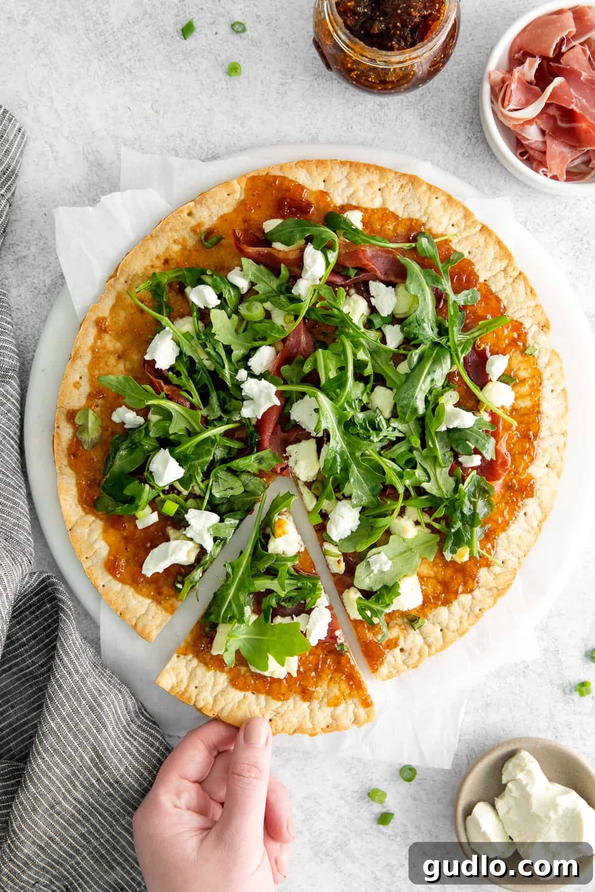 Serving a Slice of Flatbread A hand gently removing a slice of the fig and goat cheese flatbread, showcasing its crispy crust and fresh toppings.