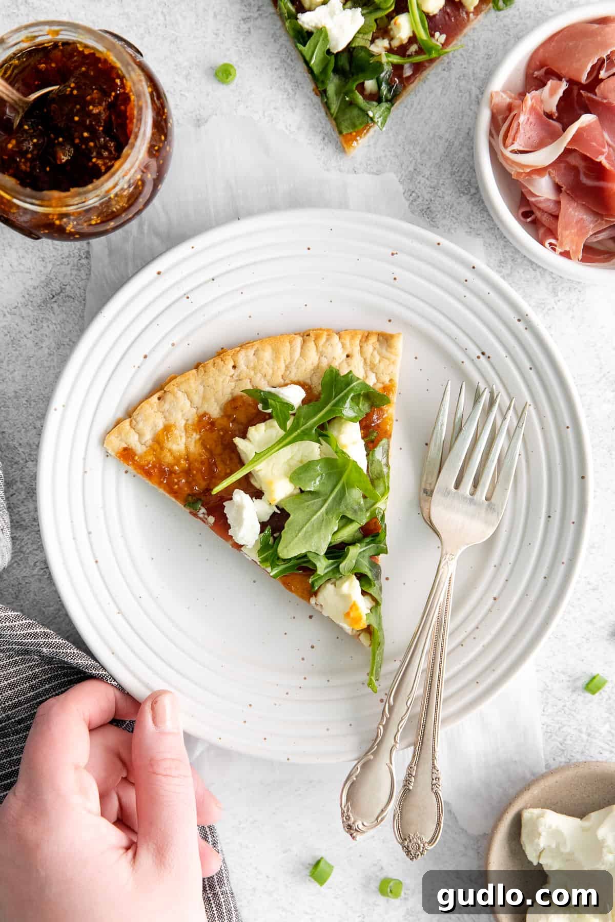 Close-up of a Fig and Goat Cheese Flatbread Slice A perfectly portioned slice of fig and goat cheese flatbread on a small plate, ready to be eaten, with forks nearby.