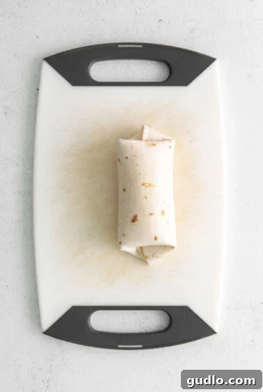 A perfectly rolled burrito on a cutting board.