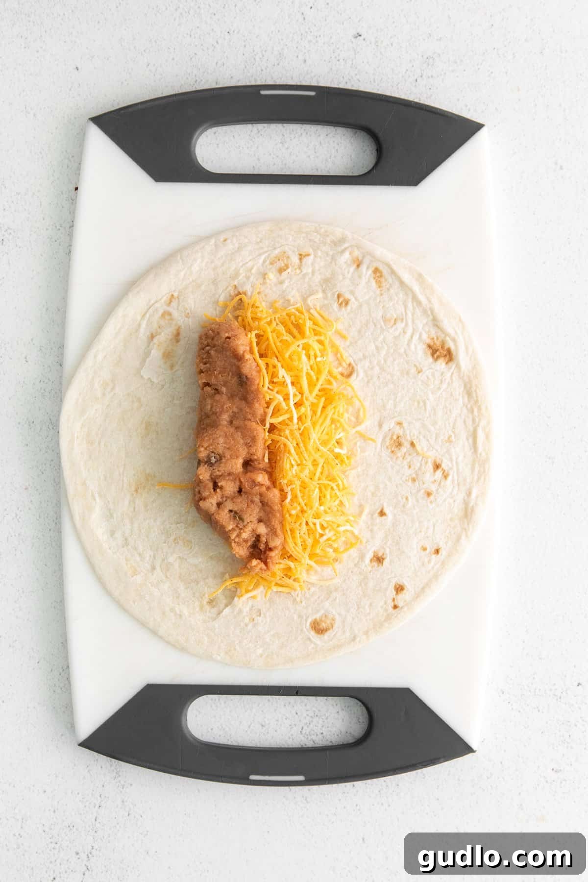 Tortilla with Cheese for Bean and Cheese Burrito An open flour tortilla topped with a generous sprinkle of shredded Mexican cheese, ready for filling.