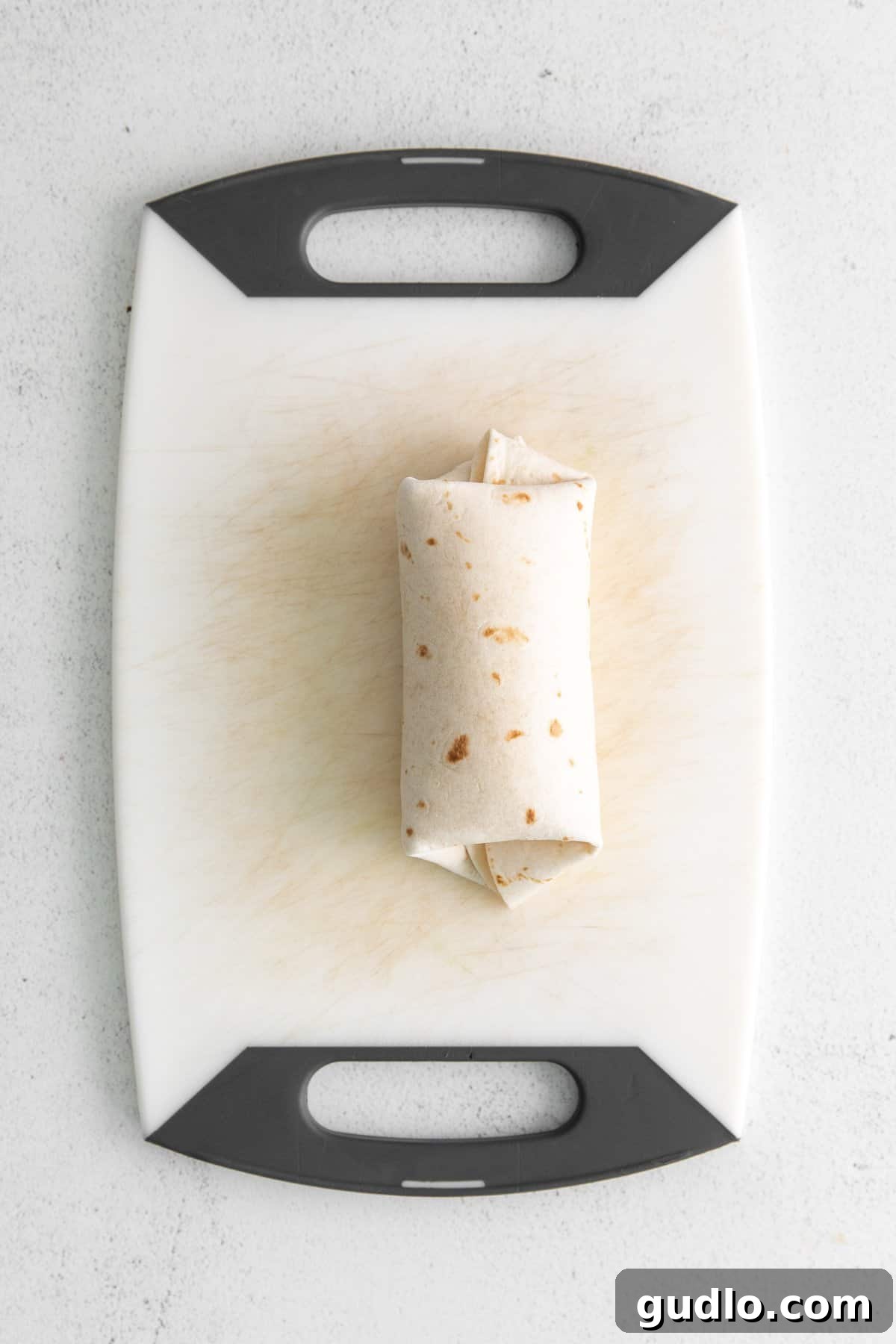 How to Roll a Bean and Cheese Burrito A freshly rolled bean and cheese burrito, sealed and ready to be cooked or frozen, resting on a cutting board.