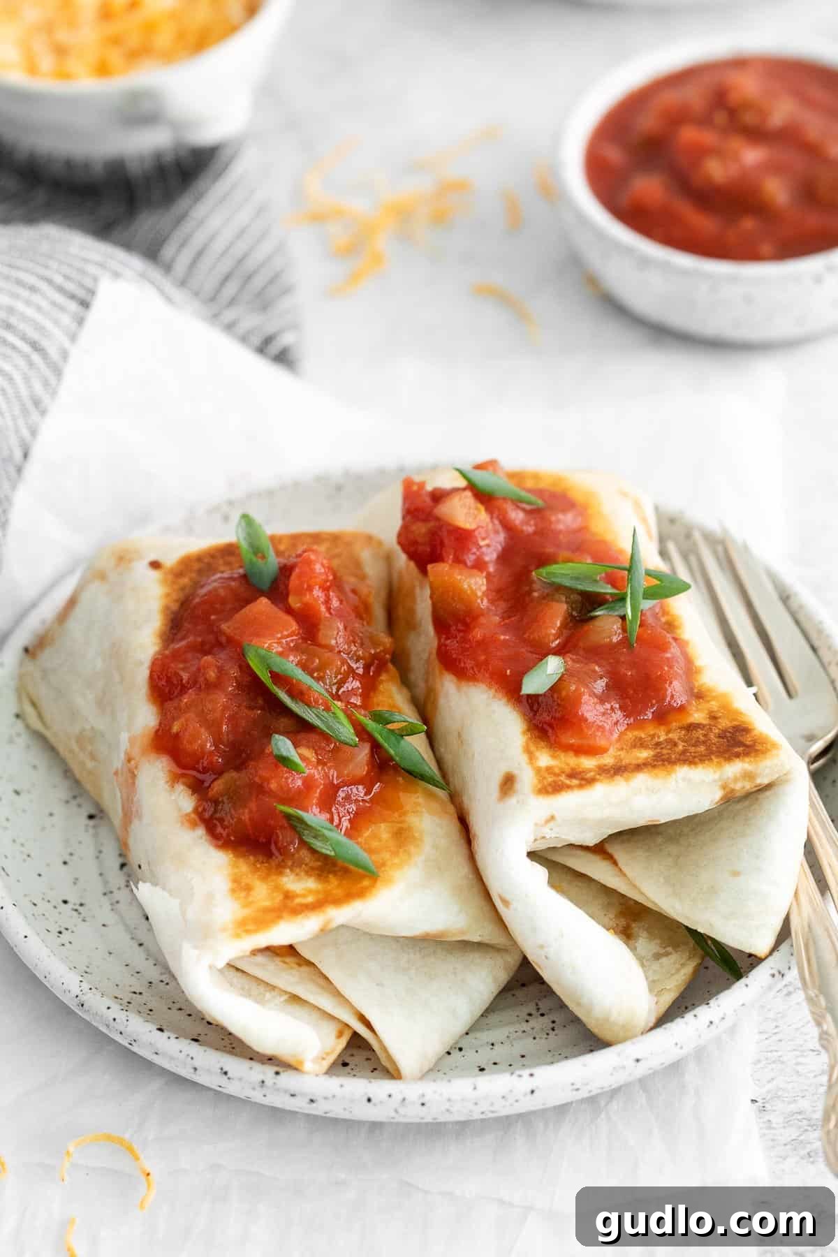 Serving Heated Bean and Cheese Burritos with Salsa Two freshly heated bean and cheese burritos, cut in half and topped with a dollop of vibrant salsa, served on a white plate.