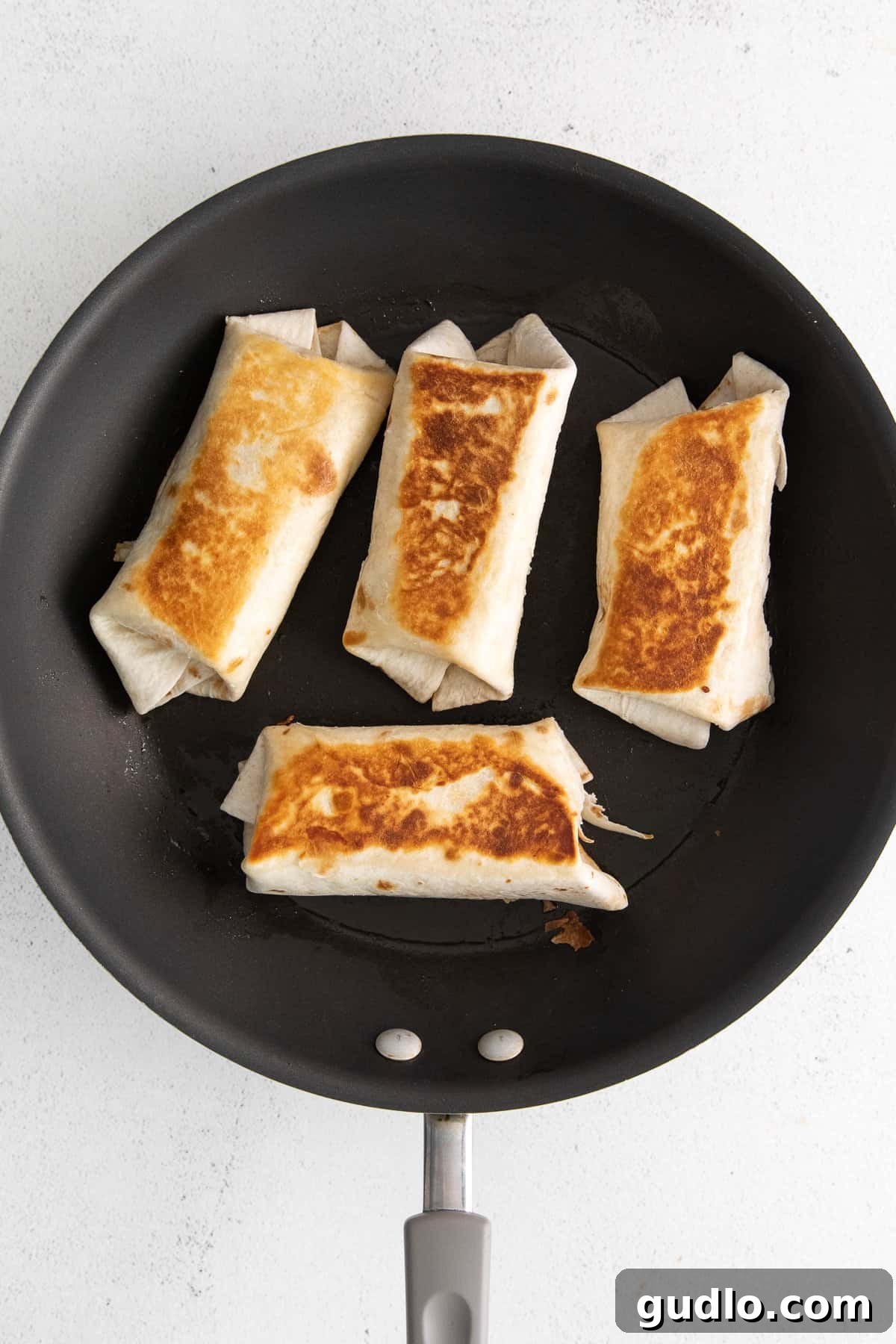 Stovetop Seared Bean and Cheese Burritos Four bean and cheese burritos sizzling in a hot skillet, developing a golden-brown crust.