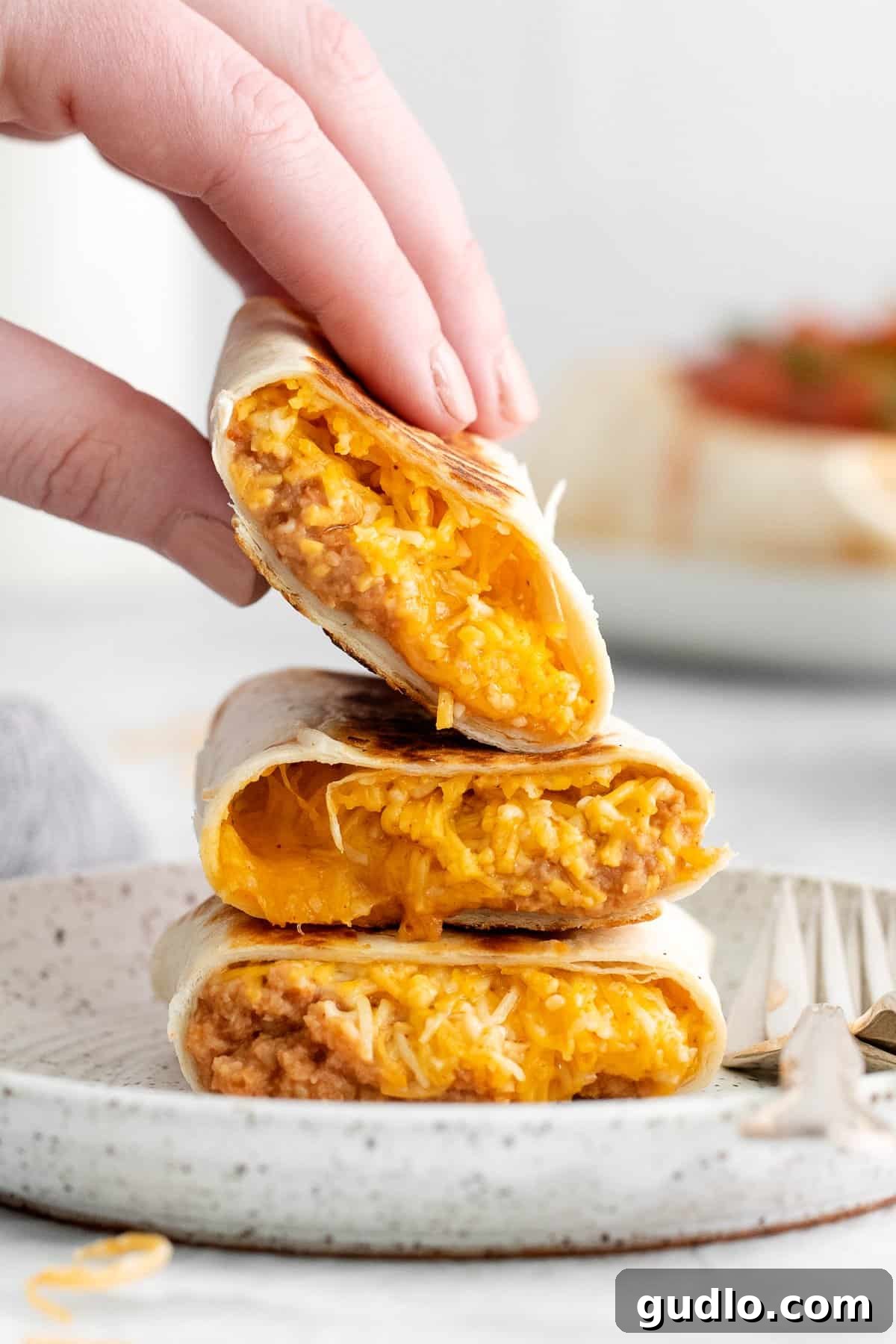 Enjoying a Delicious Bean and Cheese Burrito A hand reaching to pick up a perfectly cooked and topped bean and cheese burrito, showcasing its tempting appearance.