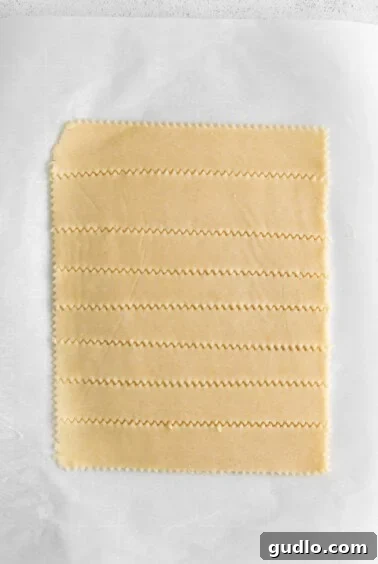 Savory Homemade Cheese Crisps 5 Thinly rolled cracker dough, perfectly seasoned and meticulously sliced into uniform cracker shapes on parchment paper.
