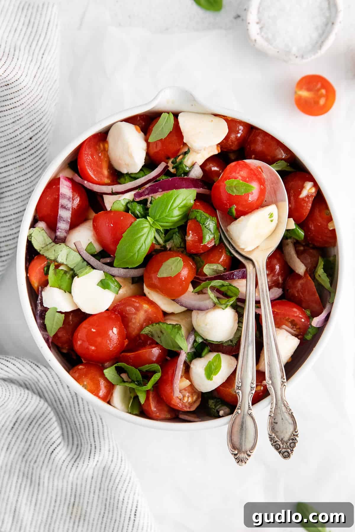 A beautifully arranged fresh tomato mozzarella salad in a large bowl with serving spoons, ready to be enjoyed.