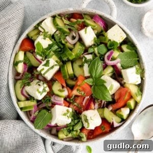 A refreshing cucumber tomato feta salad in a salad bowl, garnished with fresh herbs.