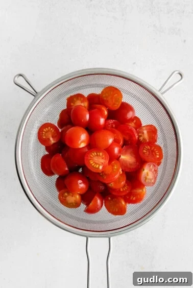 Halved cherry tomatoes in a colander, seasoned with salt.
