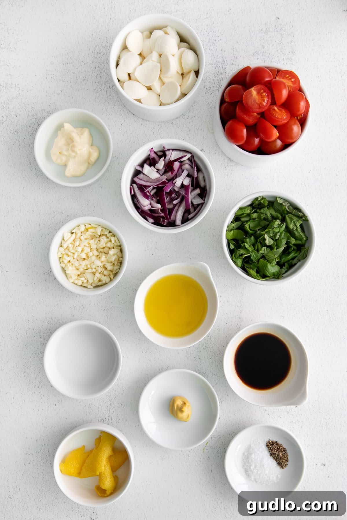 A selection of fresh ingredients laid out on a kitchen countertop, including cherry tomatoes, mozzarella balls, basil, and red onion, awaiting preparation for the salad.