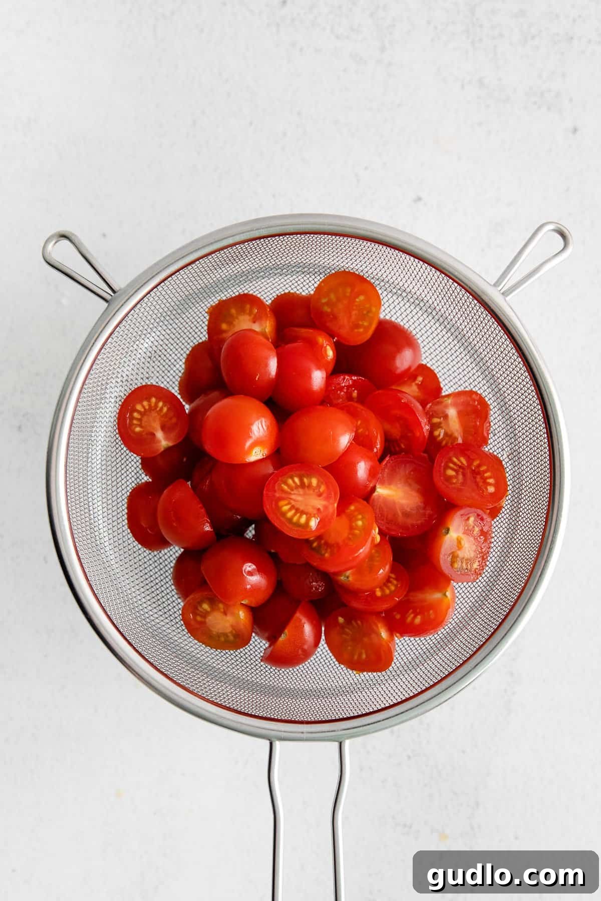 Halved cherry tomatoes in a colander, seasoned with salt, allowing excess liquid to drain, a crucial step for a non-watery salad.