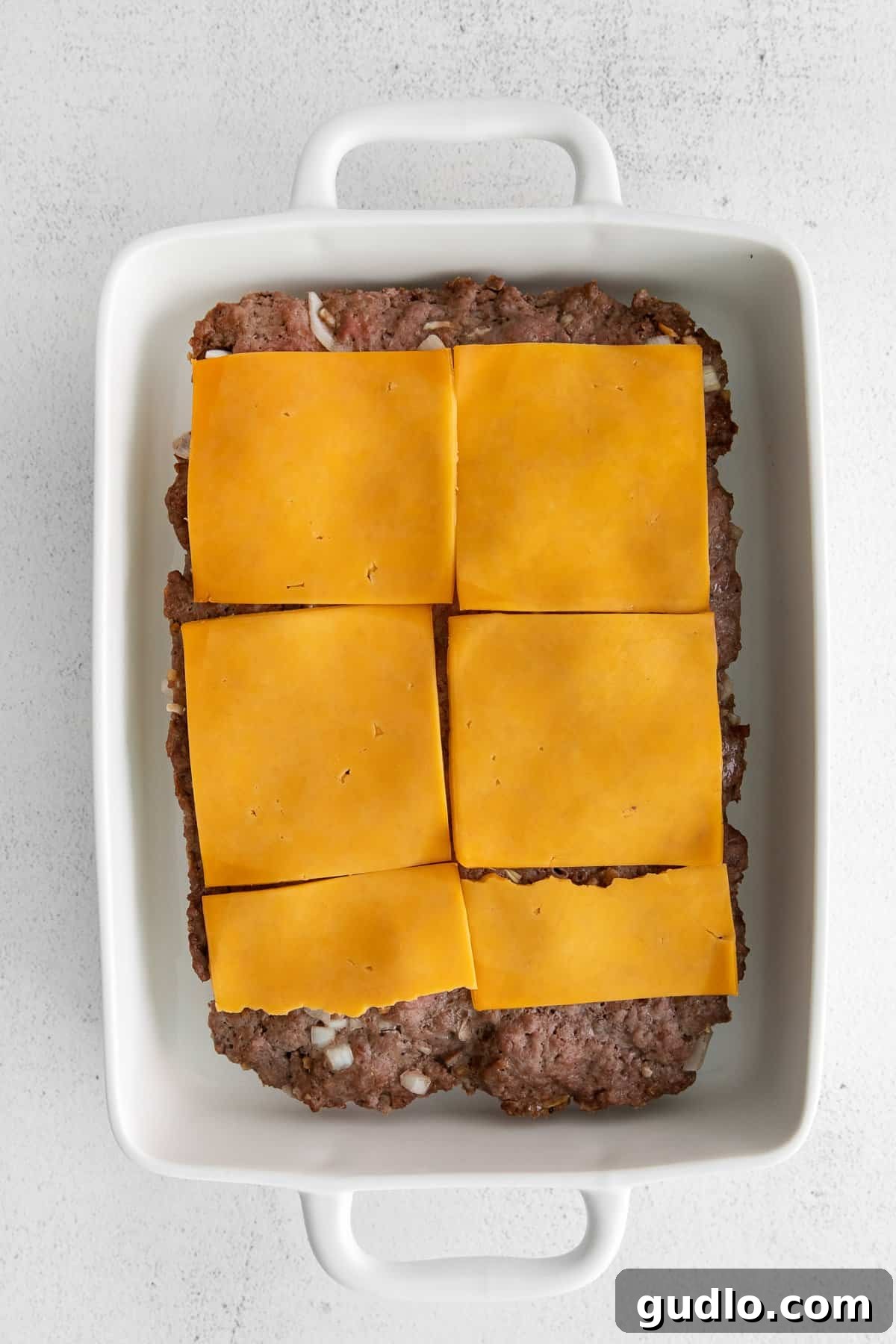 Cheesy Perfection: Hawaiian Roll Sliders Ready for the Oven Melted cheese bubbling over a giant burger patty on Hawaiian rolls.
