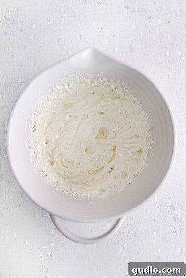 Cream cheese, sour cream, mayo, salt, and pepper being blended in a large bowl with a hand mixer.